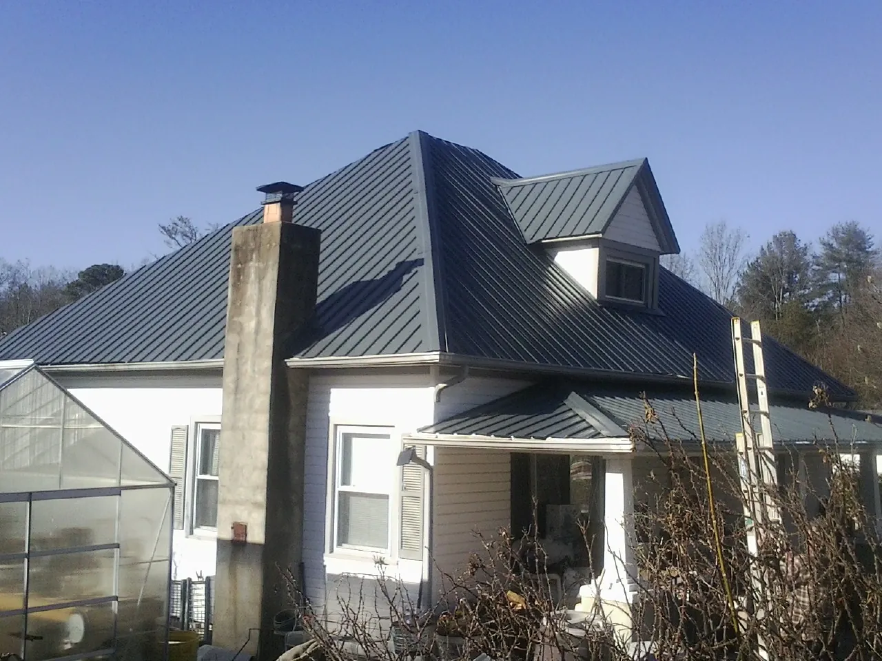 Dark blue standing seam metal roof on a white farmhouse with dormer — Slate & Tile Roof Repair by Roofing Brothers in Medicine Lodge