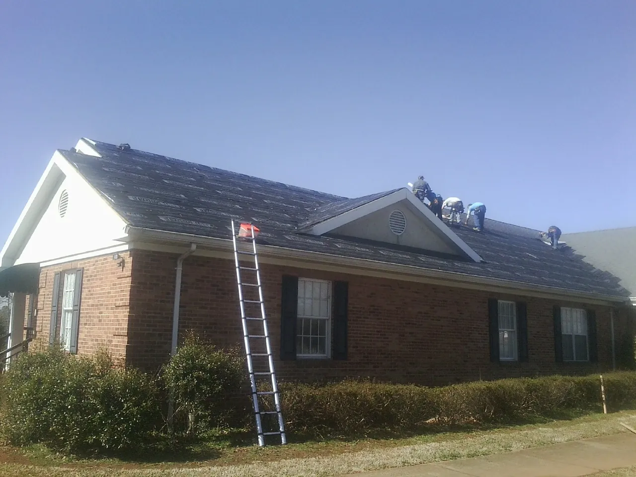 Crew tearing shingles off a brick ranch roof with a ladder set — Metal Roof Repair work by our crew in Medicine Lodge