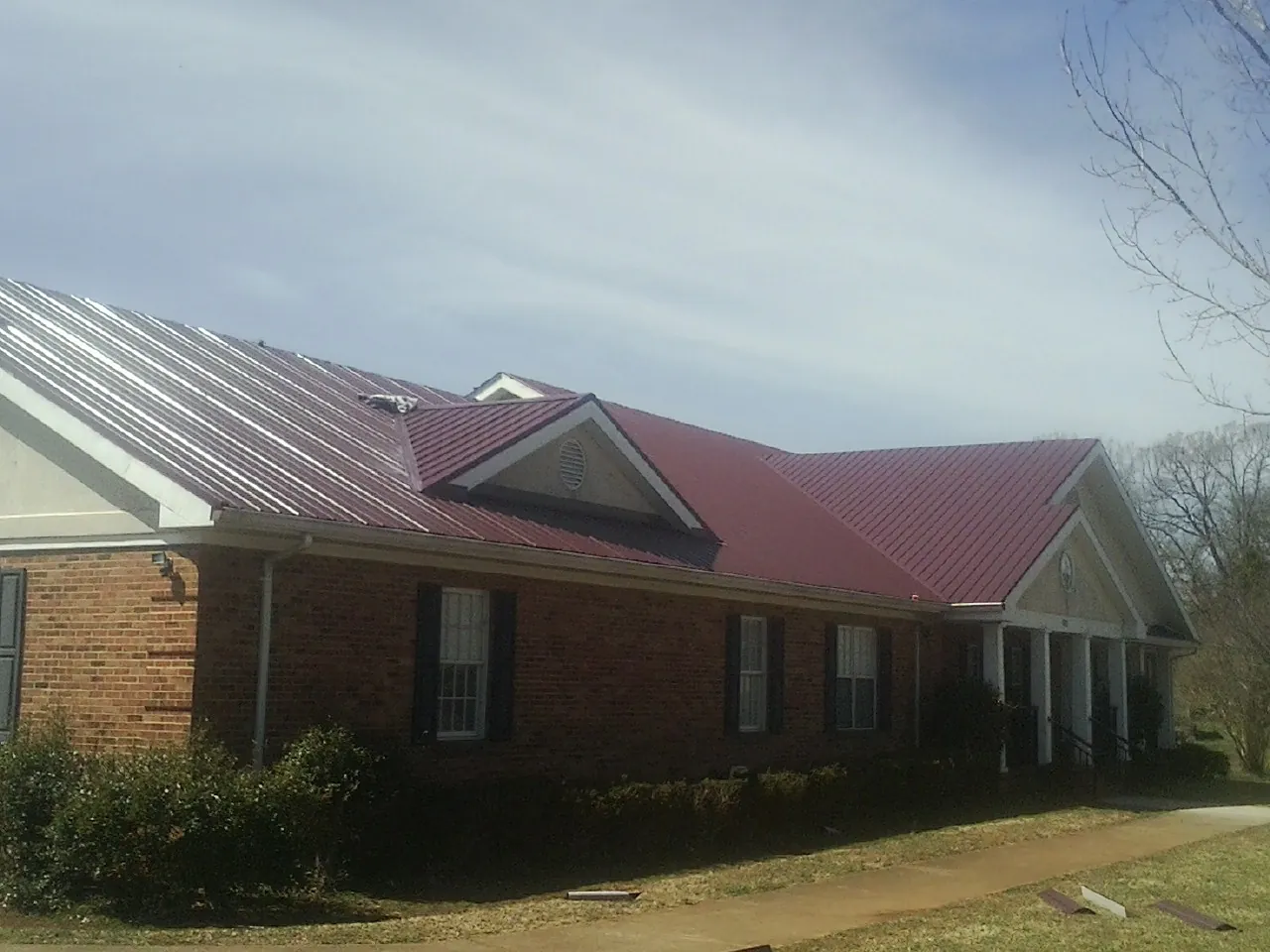 Red metal roof with gabled entries on a long brick building, from a Hail Damage Roof Repair job in Medicine Lodge