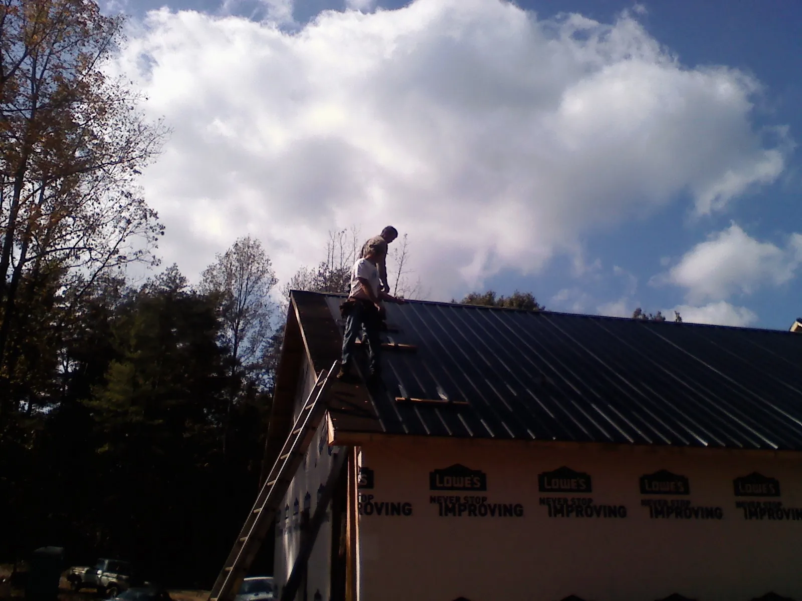Roofer fastening dark metal panels high against a cloudy sky, from a Roof Inspection job in Medicine Lodge
