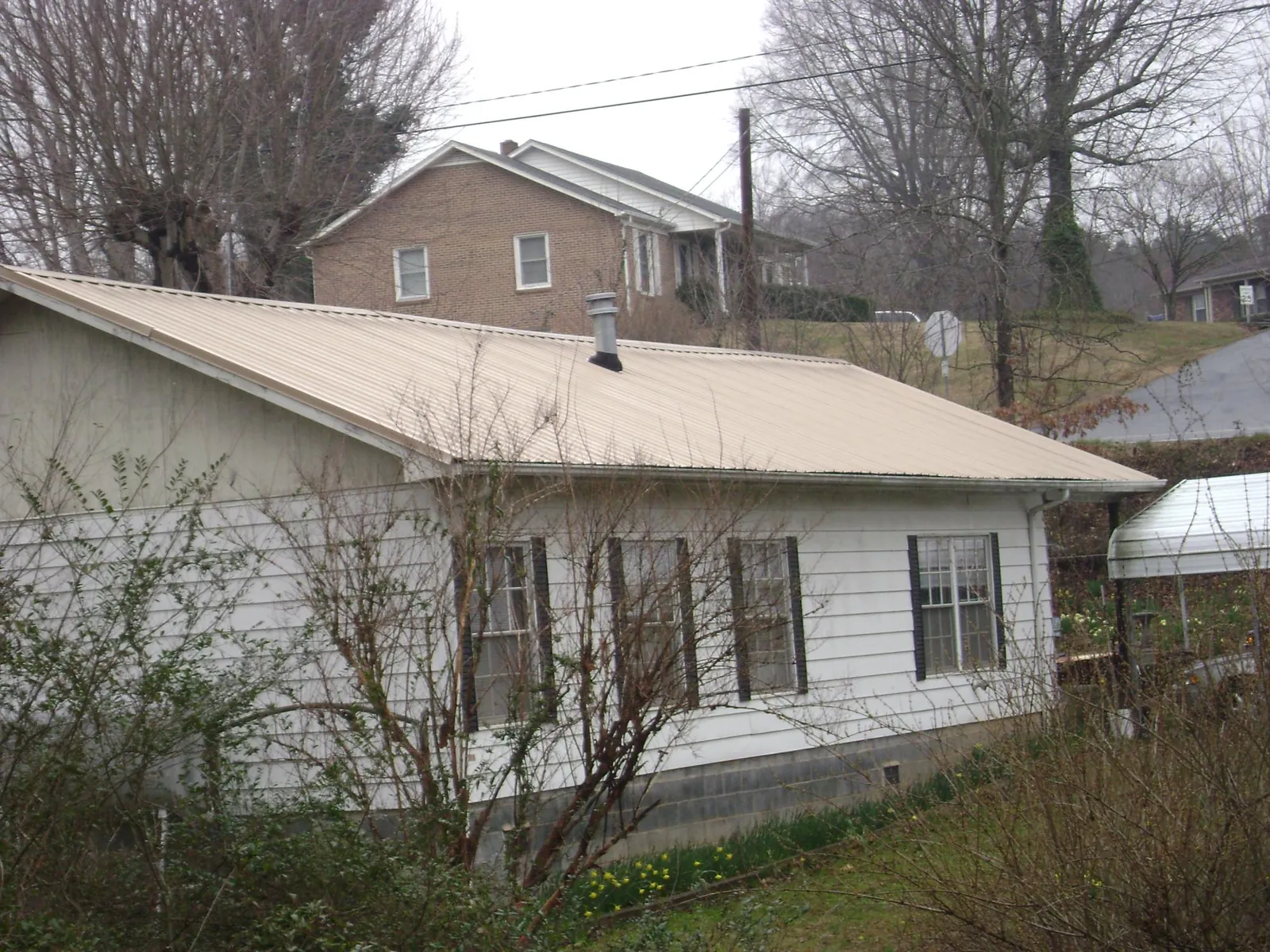 Tan metal roof on a white sided house set into a hillside — Commercial Roofing by Roofing Brothers in Medicine Lodge