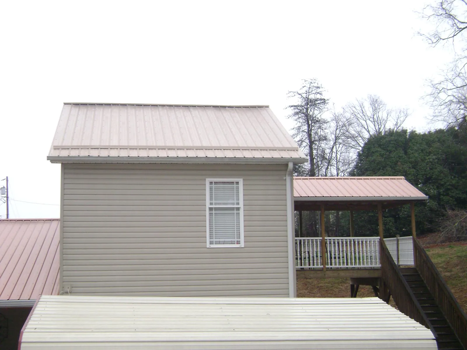 Tan metal roofs on a two story addition and attached porch, from a Roof Replacement job in Medicine Lodge